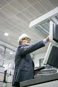 Serious mature male plant engineer operating industrial machine pushing buttons control panel holding tablet copy